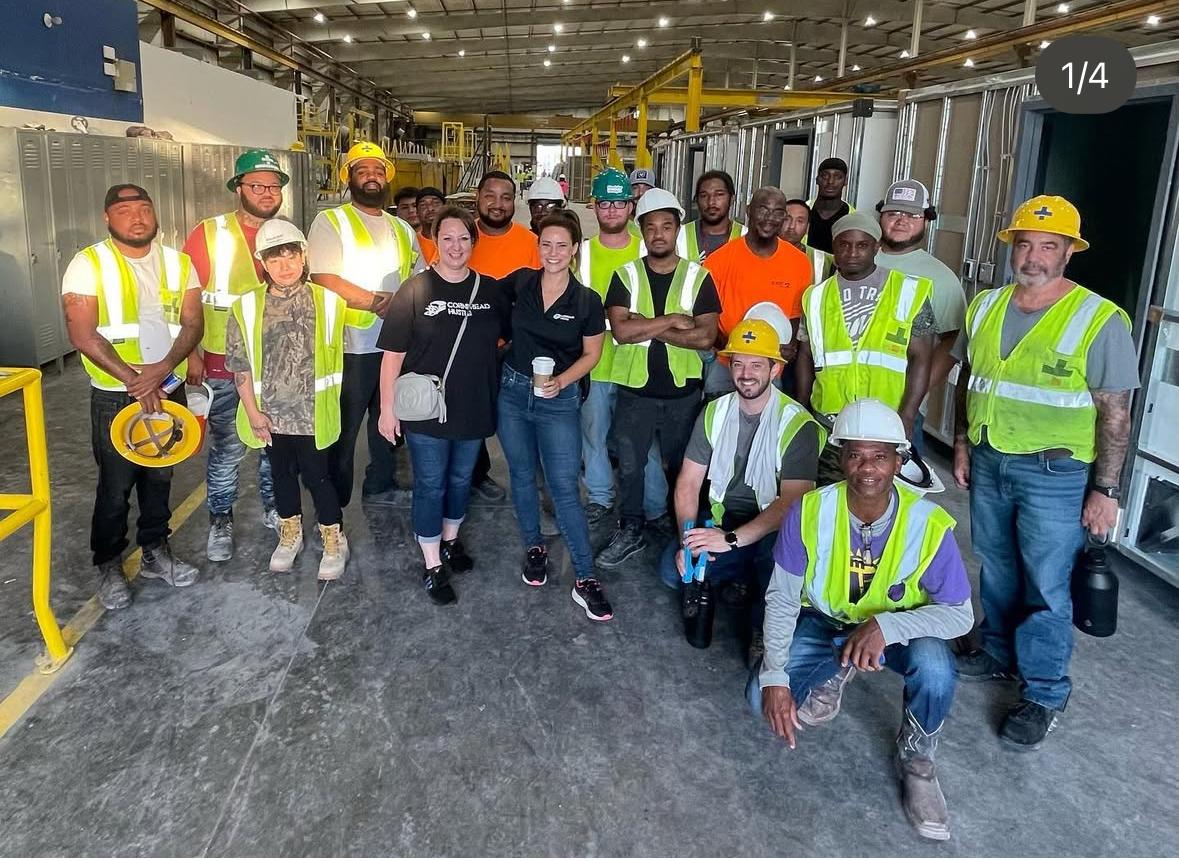 Woman in black surrounded by people in hard hats