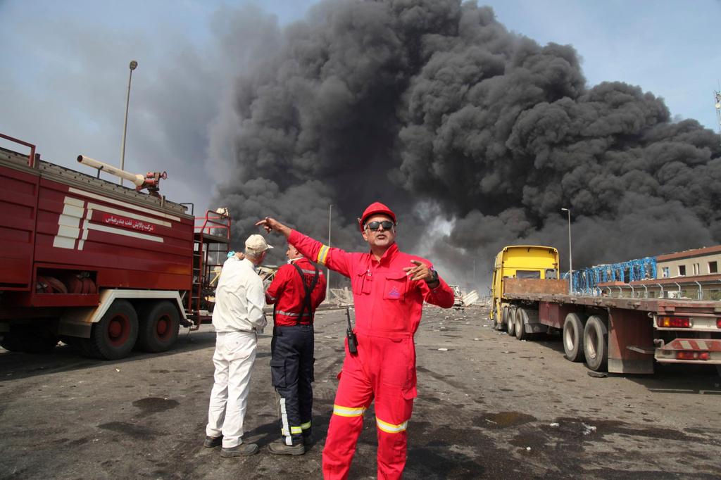 Firefighters work as black smoke rises in the sky after a massive explosion rocked a port near the southern city of Bandar Abbas, Iran