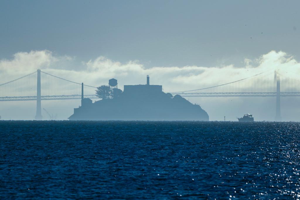 A boat makes its way toward Alcatraz Island with the San Francisco-Oakland Bay Bridge in the background 