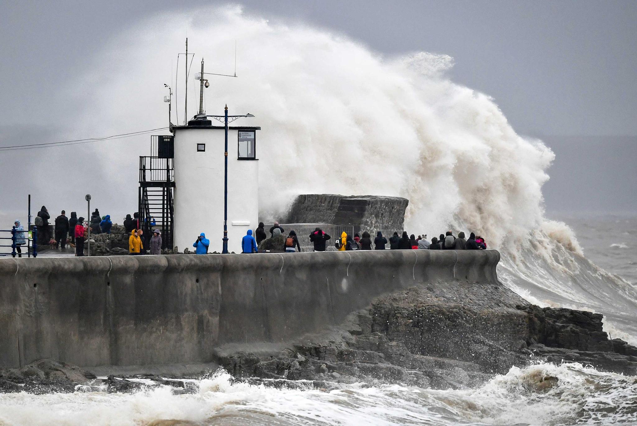 People watch waves and rough seas pound against the harbour wall