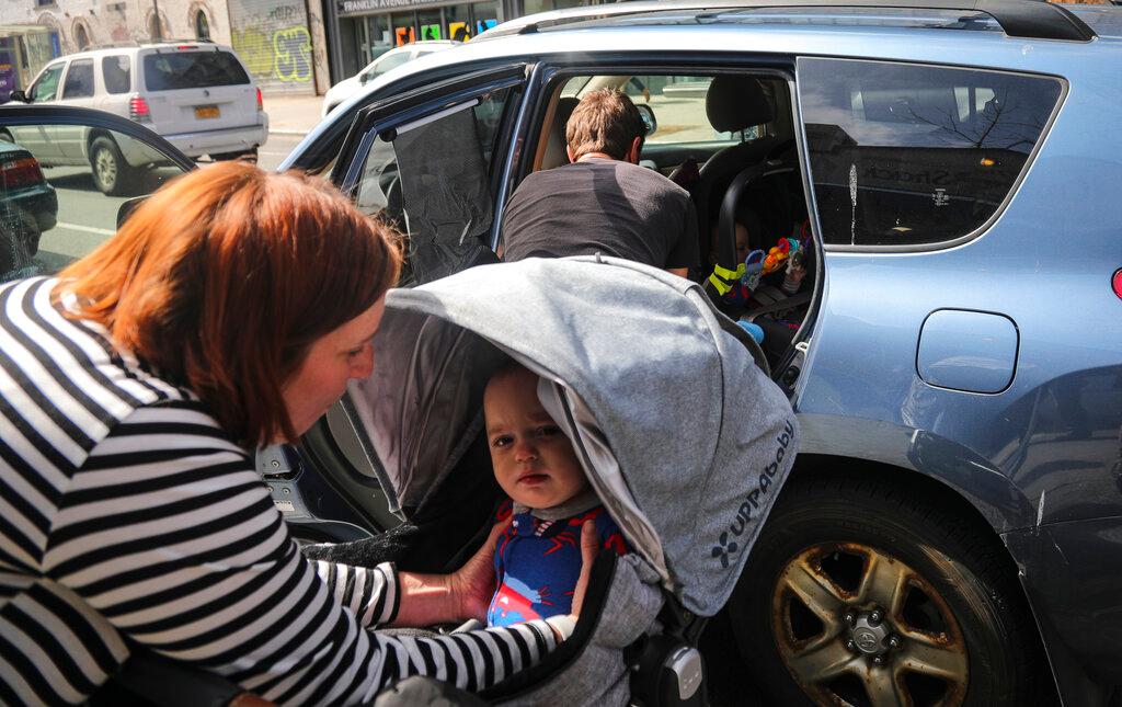 While Justin Bracken packs the family car, Cailin Sandvig, left, lifts their 10-month old son Milo from his stroller to join his twin inside the car, as they prepare to leave home in the Crown Heights neighborhood of the Brooklyn borough of New York to avoid the spread COVID-19, Monday March 16, 2020. "We are fleeing the city," said Sandvig who works remotely for her job. "We are going to end up in Wheaton, Illinois, where we have a big old house to be in with my mom that's otherwise empty." Bracken added that from following the news "its been clear for a while that things are getting pretty serious—especially from Italy, it seems pretty eminent that things are about to get bad here."