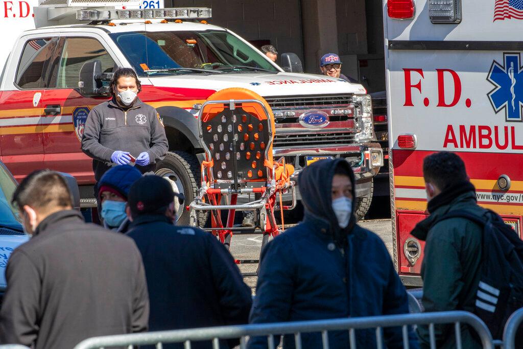 An Emergency Medical Technician works as people line up outside Elmhurst Hospital Center to be tested for the coronavirus in Queens