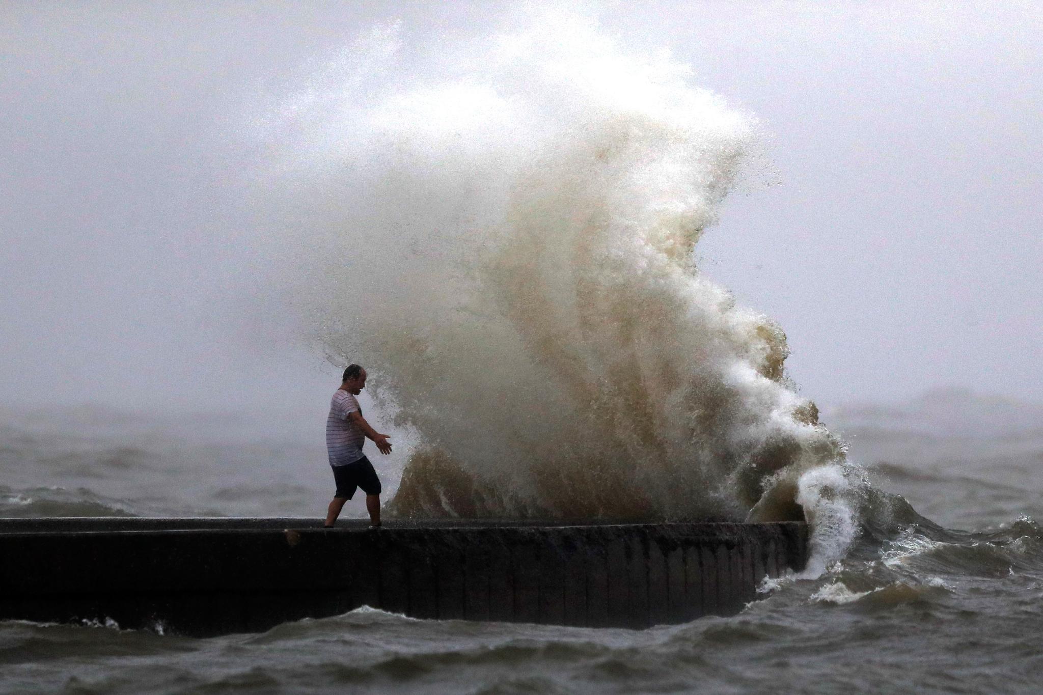 A wave crashes as a man stands on a jetty near Orleans Harbor in Lake Pontchartrain