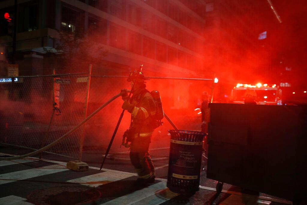 Firefighters put out a dumpster fire as protesters and police gather at Lafayette Park near the White House 