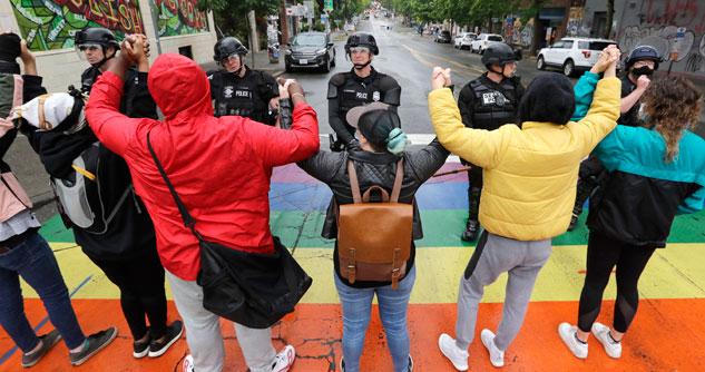 Protesters standing with hands held up in the air, facing police