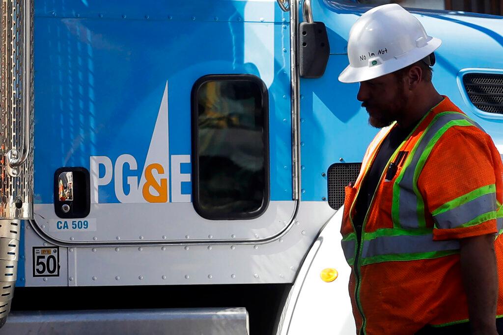 In this Aug. 15, 2019 file photo, a Pacific Gas & Electric worker walks in front of a truck in San Francisco. Pacific Gas & Electric has emerged from a contentious bankruptcy saga that began after its long-neglected electrical grid ignited wildfires in California that killed more than 100 people. PG&E announced Wednesday, July 1, 2020, it emerged from Chapter 11 bankruptcy and paid $5.4 billion in initial funds and 22.19 percent of its stock into a trust for victims of wildfires caused by its outdated equipment.