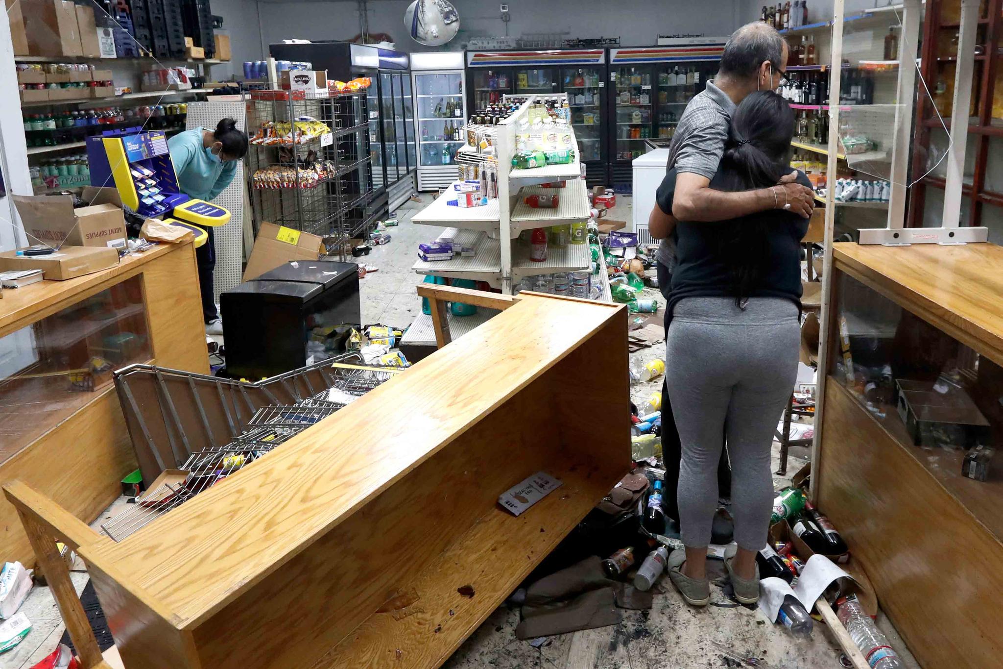 Yogi Dalal hugs his daughter Jigisha as his other daughter Kajal, left, bows her head at the family food and liquor store Monday, Aug. 10, 2020, after the family business was vandalized in Chicago.