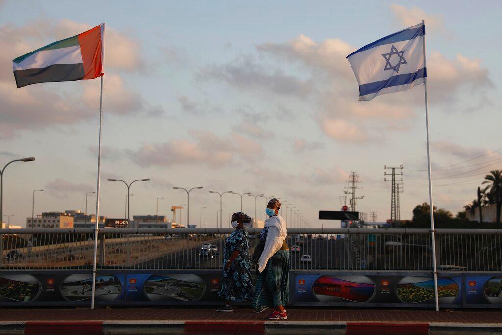 Women wearing face masks against the coronavirus walk past United Arab Emirates and Israeli flags at the Peace Bridge in Netanya, Israel, Sunday, Aug. 16, 2020. The UAE flag was displayed to celebrate last week's announcement that Israel and the United Arab Emirates have agreed to establish full diplomatic relations