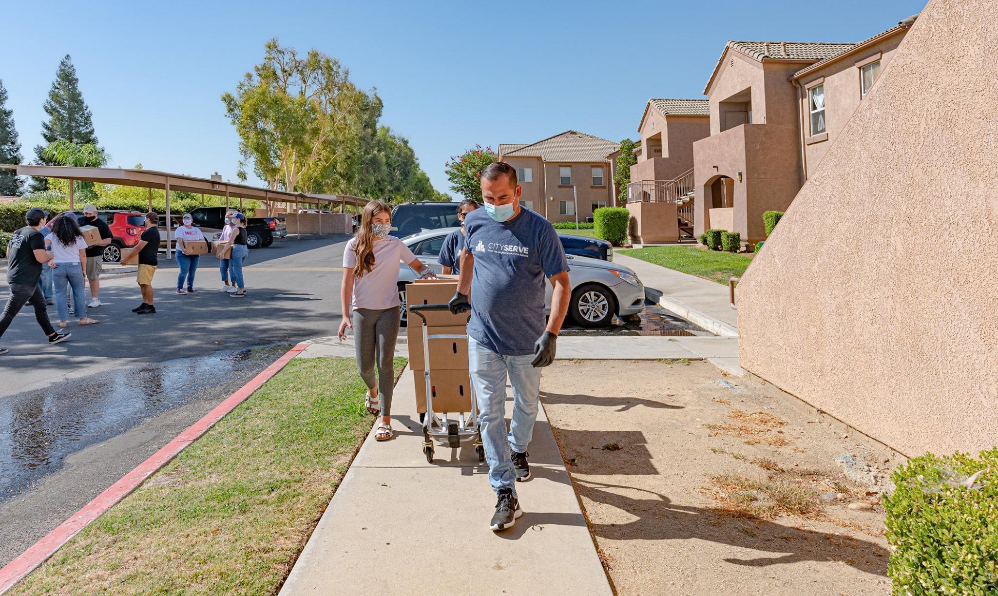 People walking down sidewalk delivering cart of goods