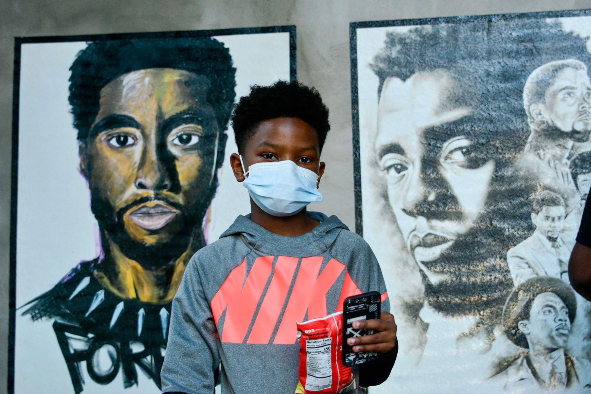 A boy stands in front of two paintings of Chadwick Boseman