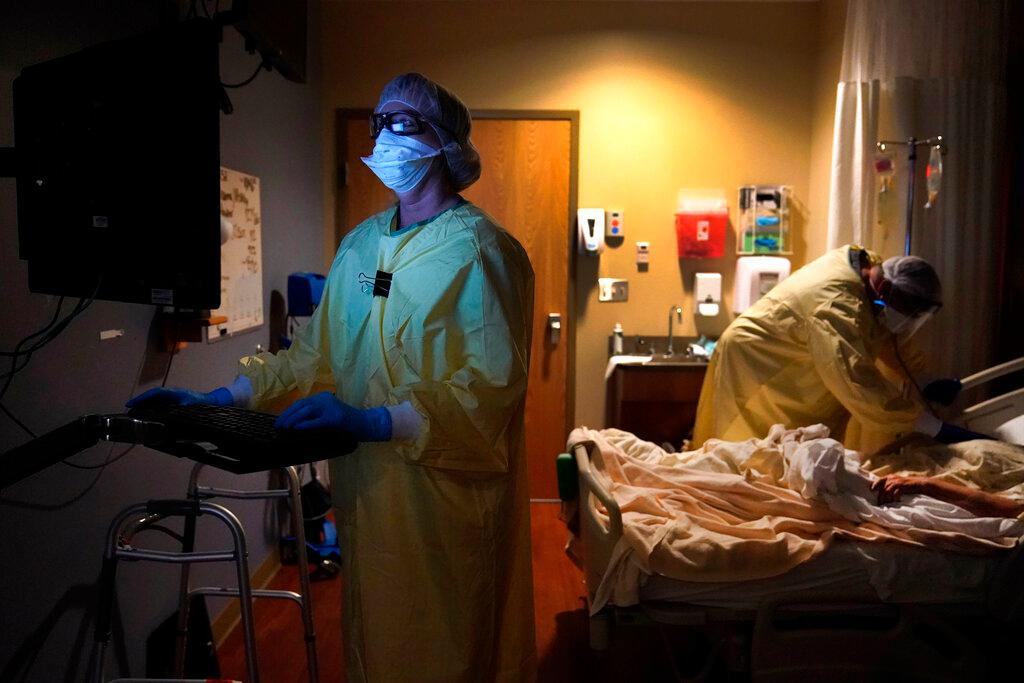Registered nurse Shelly Girardin, left, is illuminated by the glow of a computer monitor as Dr. Shane Wilson examines COVID-19 patient Neva Azinger inside Scotland County Hospital in Memphis, Mo.
