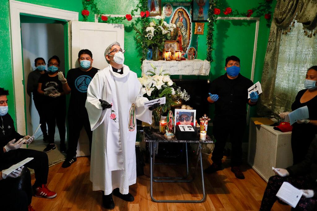 Rev. Fabian Arias performs an in-home service beside the remains of Raul Luis Lopez who died from COVID-19 