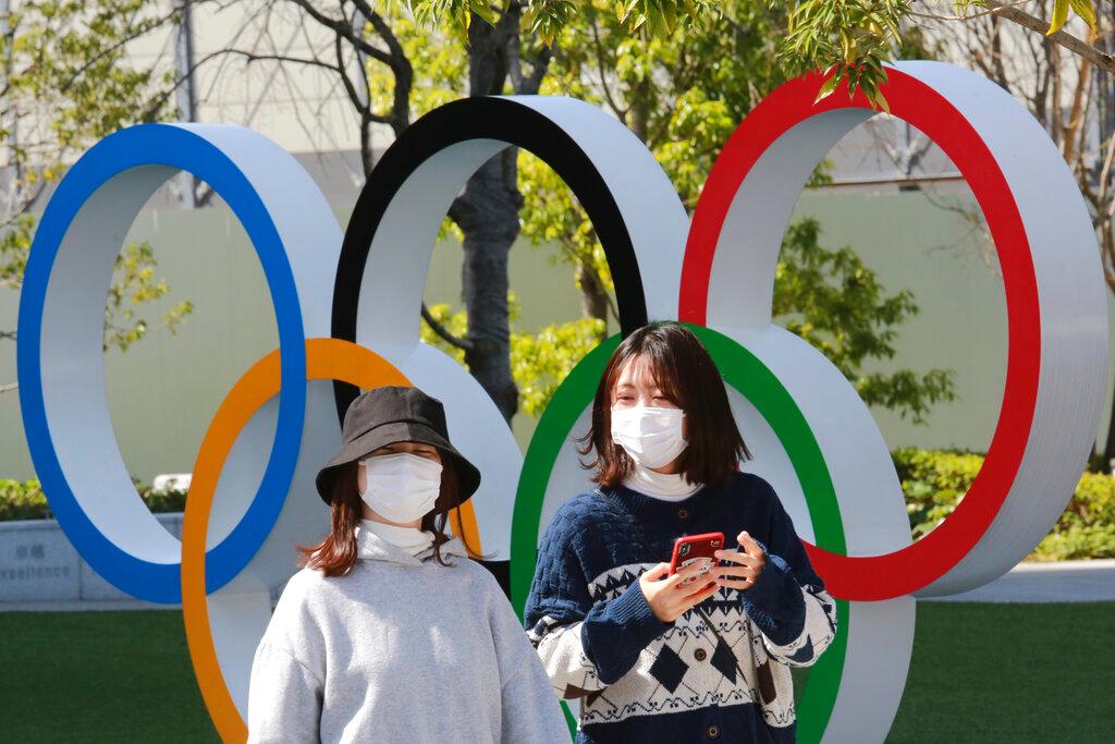 people waking in front of Olympic rings