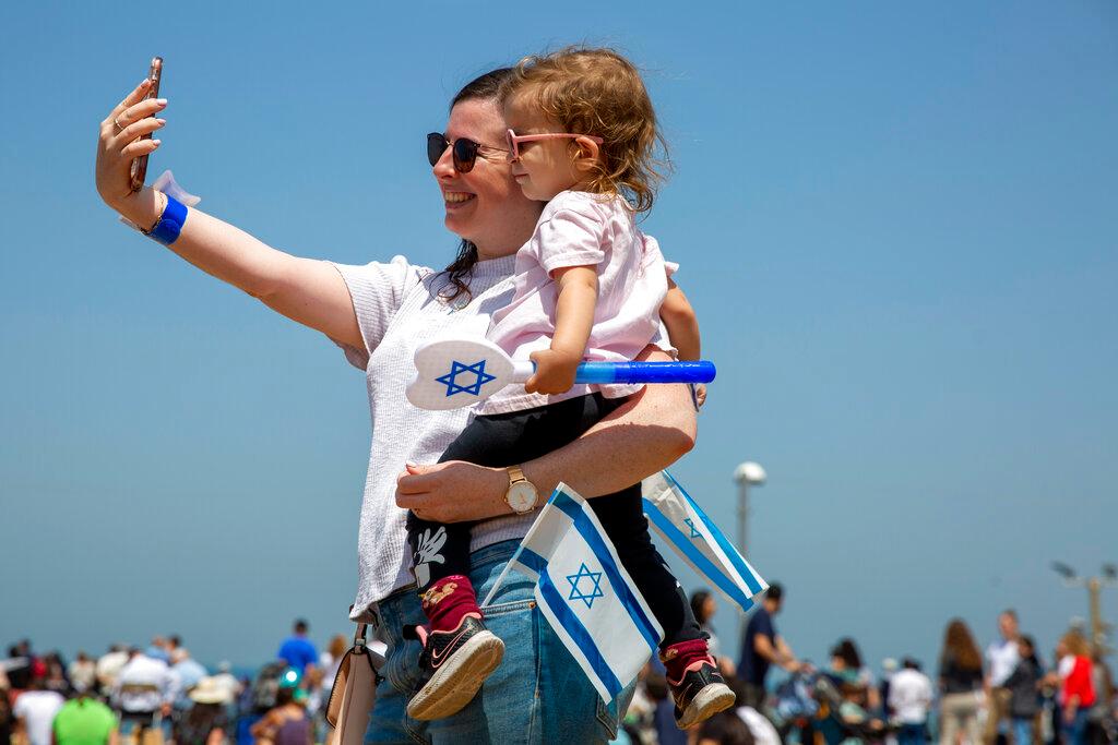 A woman smiles as she holds her child and Israeli flags during Independence Day celebrations, in Tel Aviv