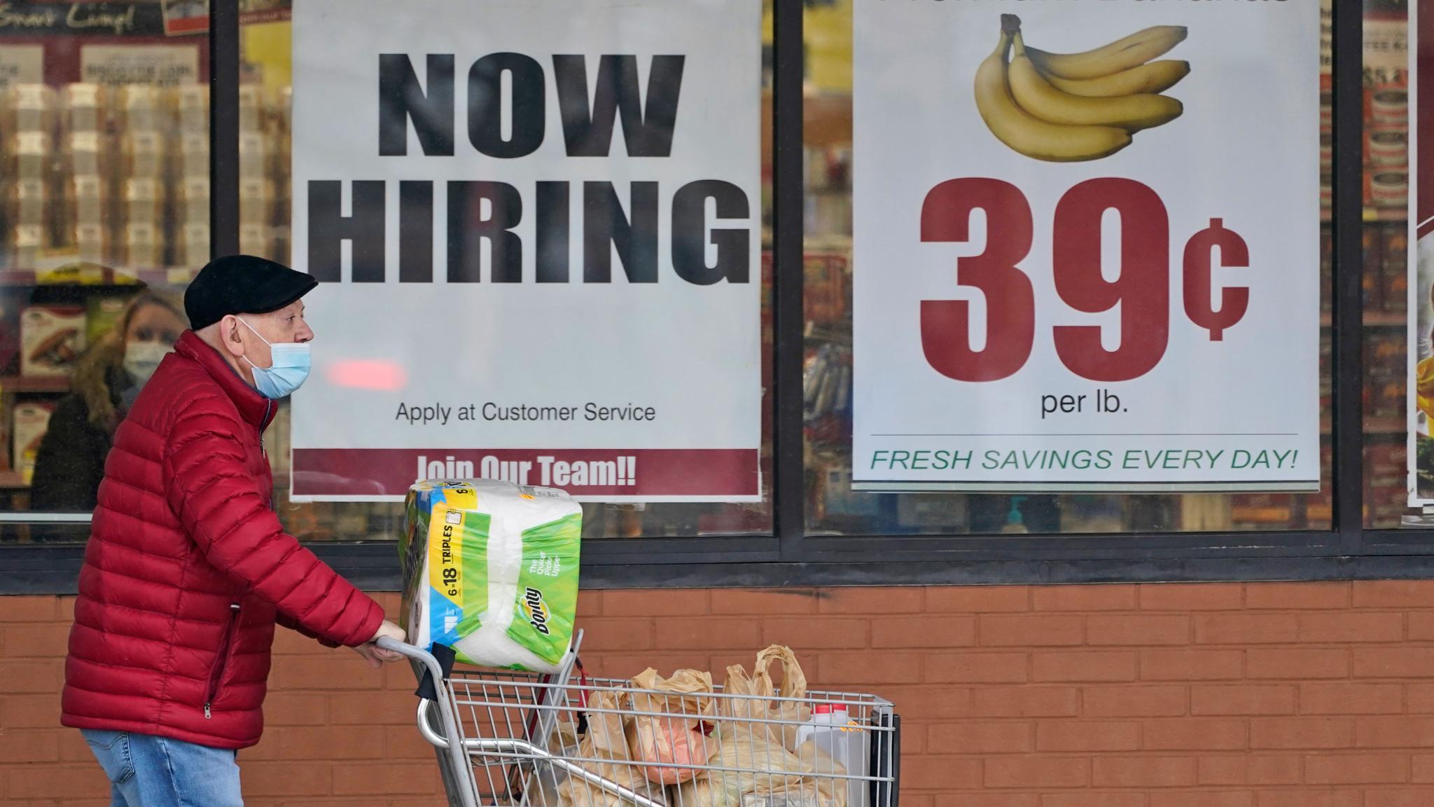 A man walks near a now hiring sign