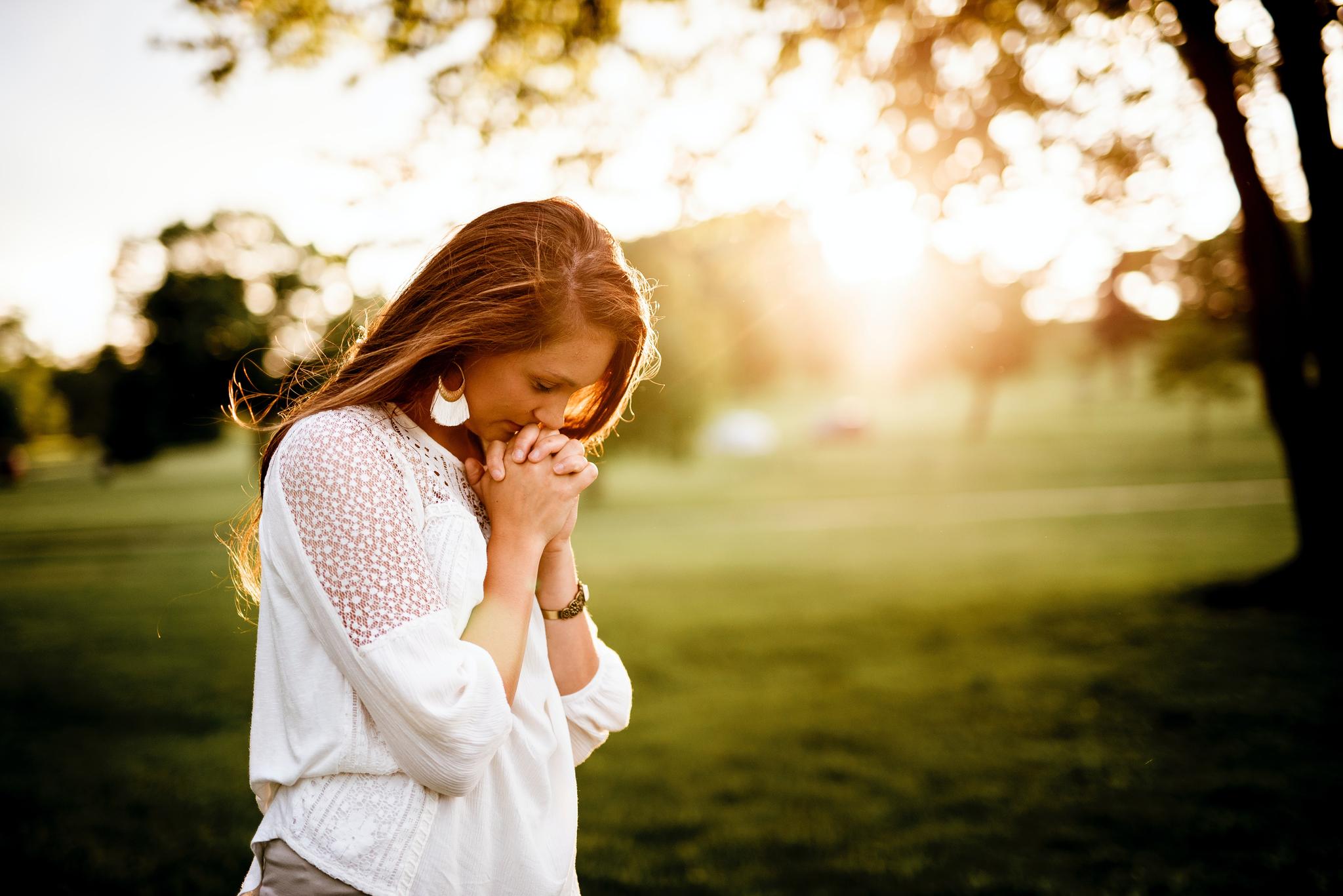 Woman standing alone in field, hands clasped at chin