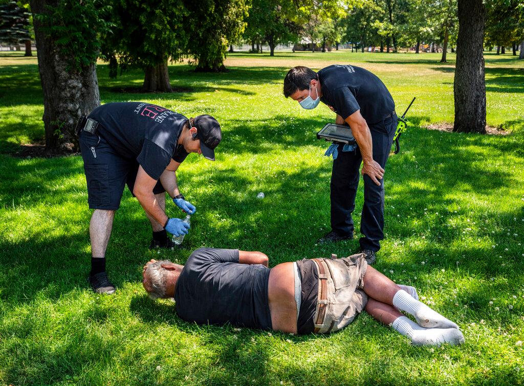 With the temperature well over 100 degrees, Spokane, Wash., firefighter Sean Condon, left and Lt. Gabe Mills, assigned to the Alternative Response Unit of of Station 1, check on the welfare of a man in Mission Park in Spokane, Wash., 