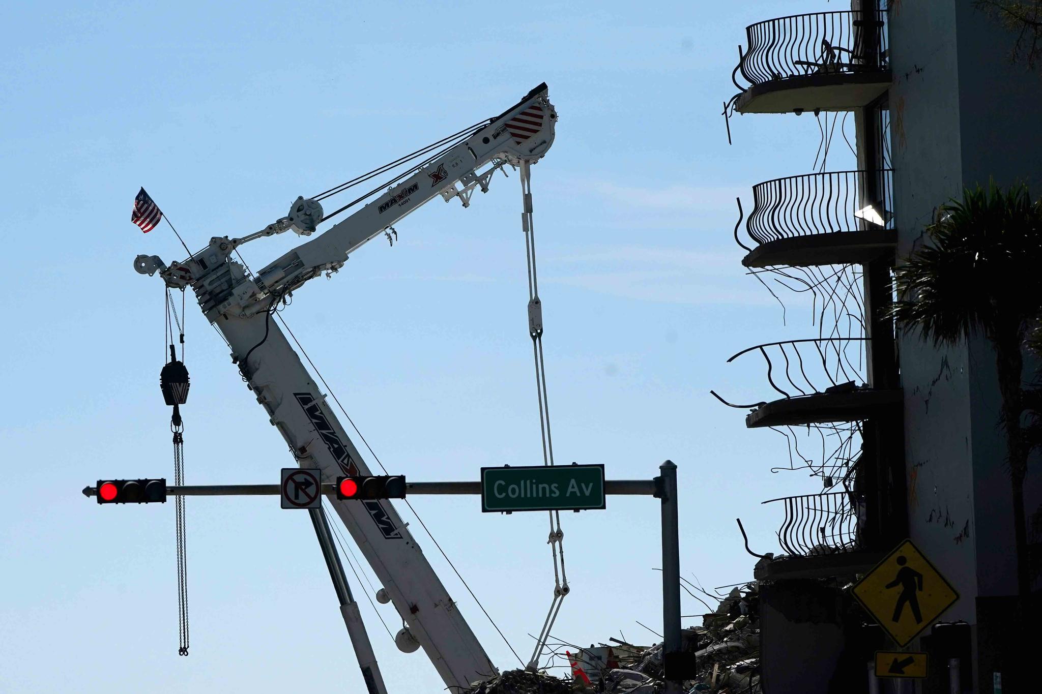 An American flag flies from a crane next to the Champlain Towers South condo building, where scores of victims remain missing more than a week after it partially collapsed, Sunday, July 4, 2021, in Surfside, Fla. Demolition teams are preparing to bring down the unstable remainder of the structure ahead of a tropical storm.