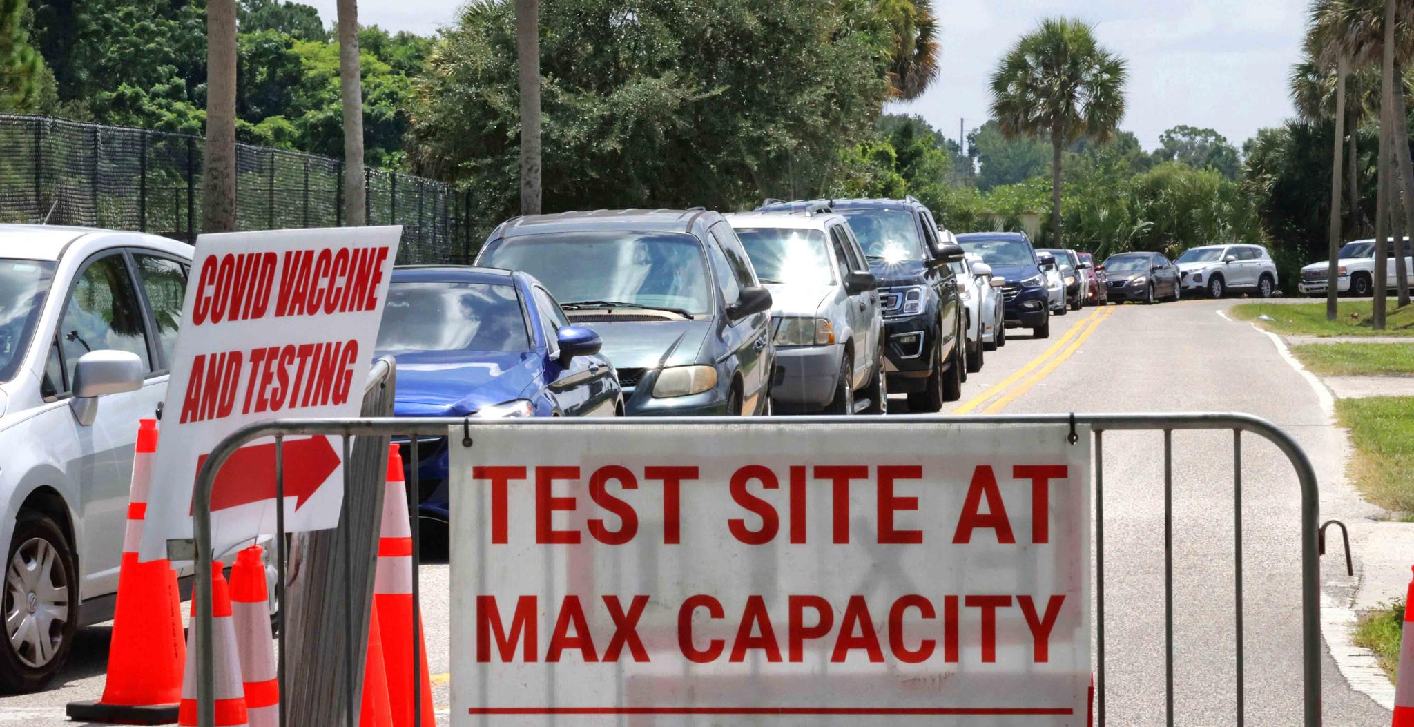 Signage stands at the ready (foreground) in case COVID-19 testing at Barnett Park reaches capacity, as cars wait in line in Orlando, Fla.