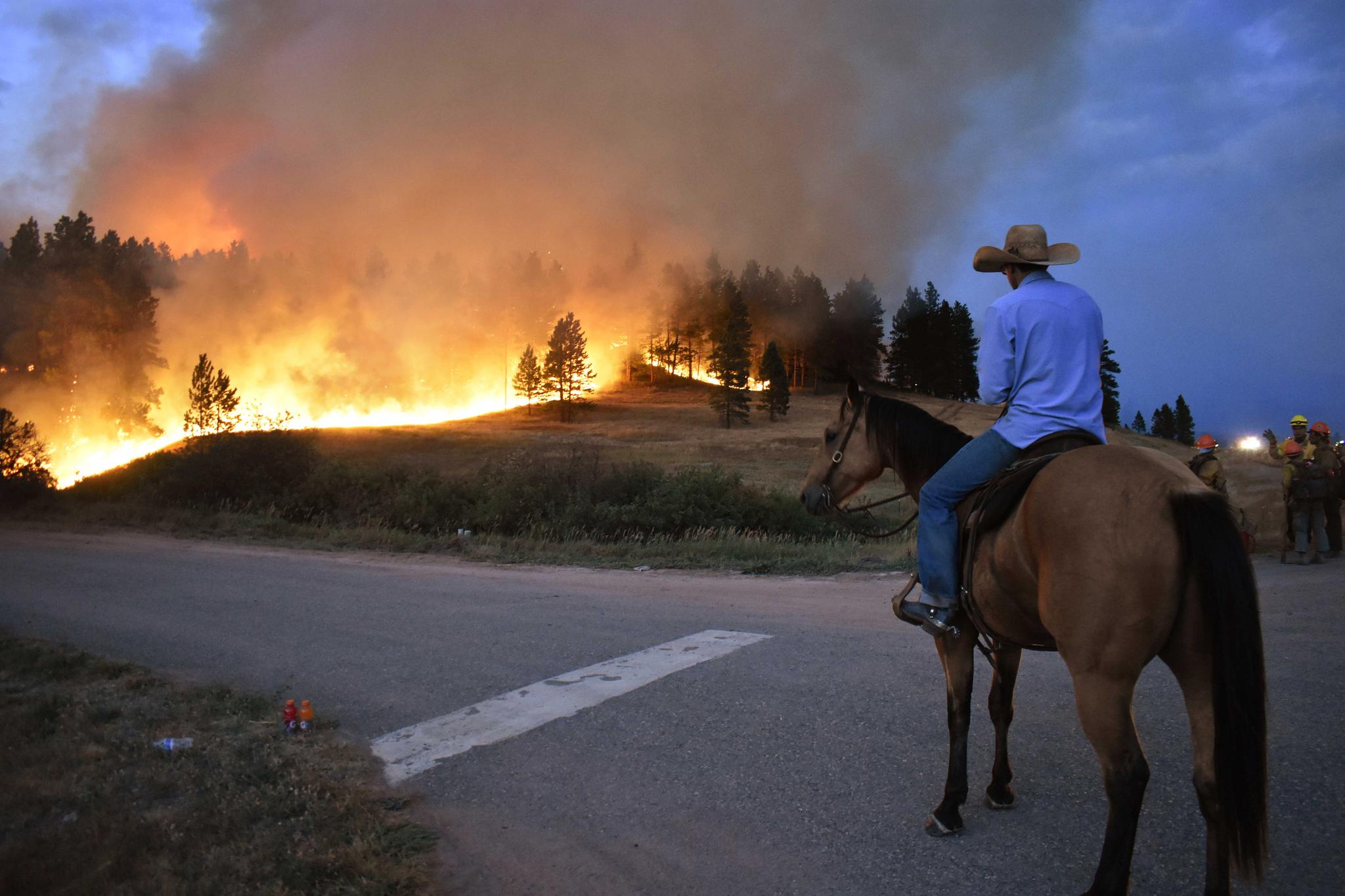 man watches from atop his horse as a hillside burns