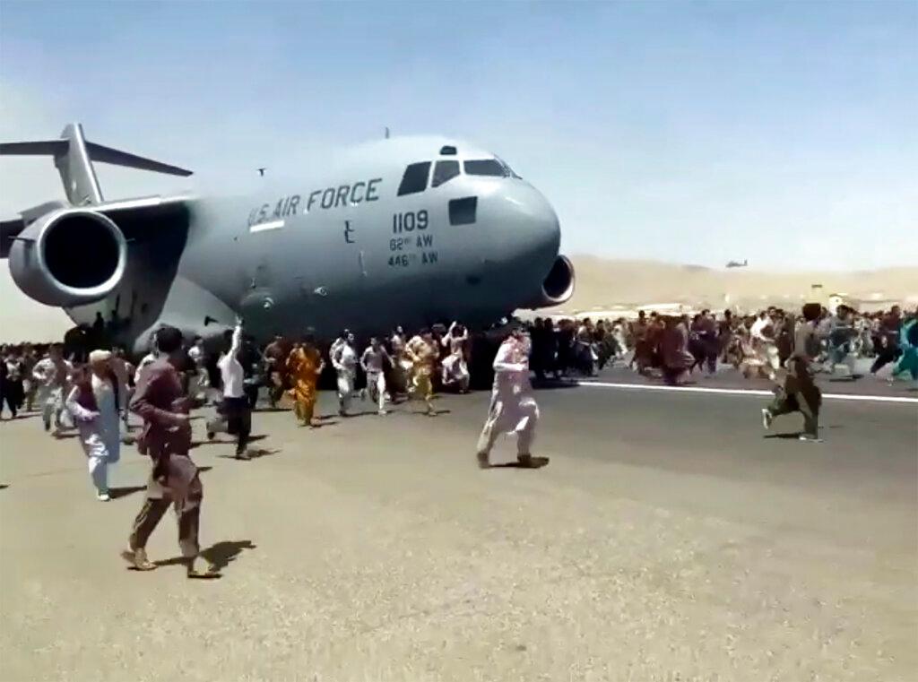 Hundreds of desperate Afghans people run alongside a USAF C-17 transport plane as it moves down a runway of the international airport, in Kabul, Afghanistan