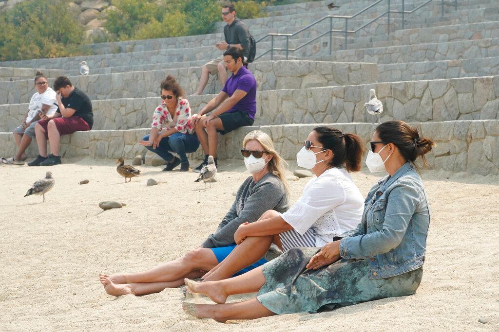 Amanda Abel, left, Kristy Weaver, center, and Kerry Murphy wear face masks as they sit along the shore of Lake Tahoe