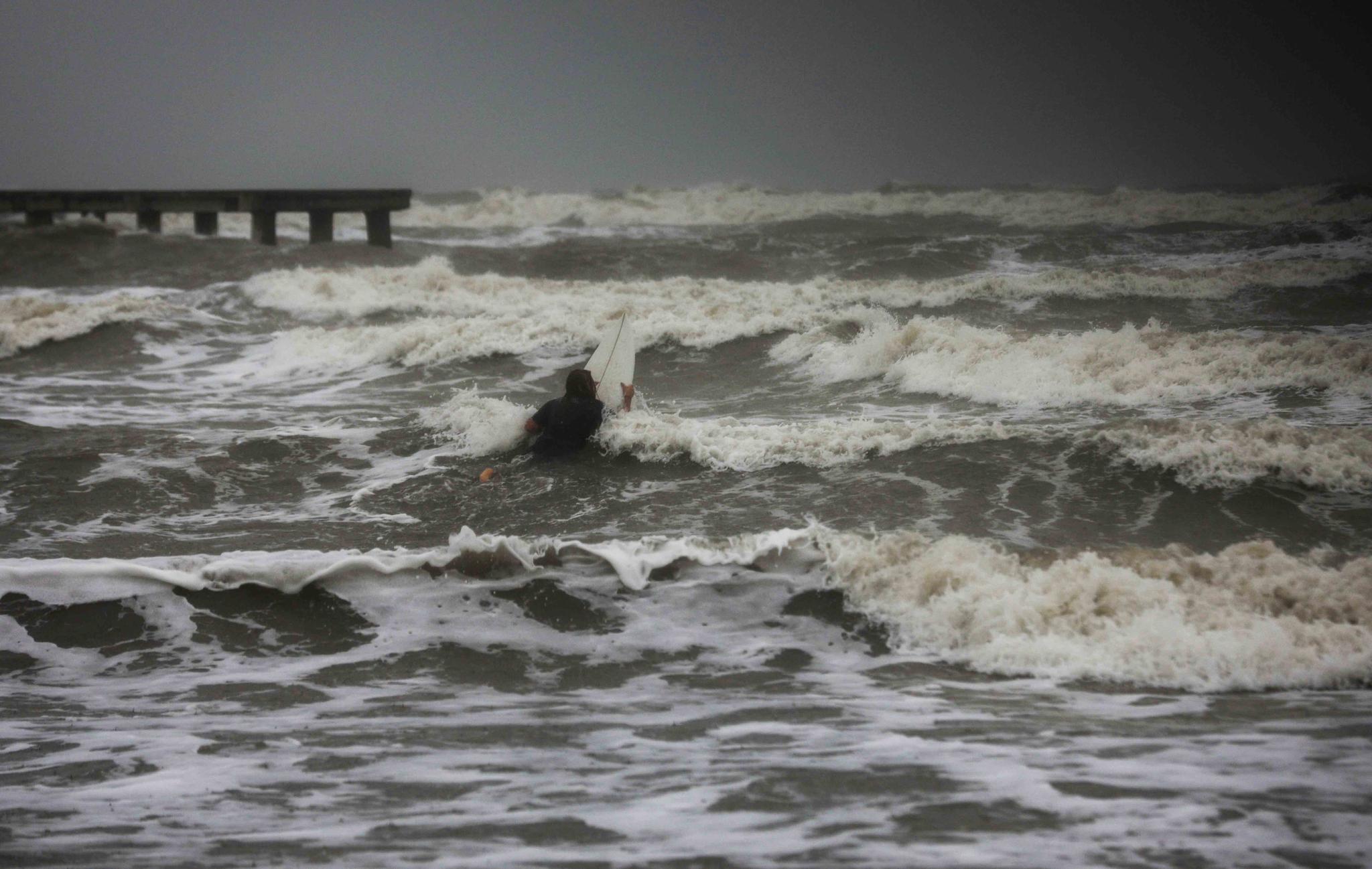 A surfer tries to paddle through the surf as wind and rain from Tropical Storm Nicholas batters the area Monday, Sept. 13, 2021, along the seawall in Galveston, Texas.