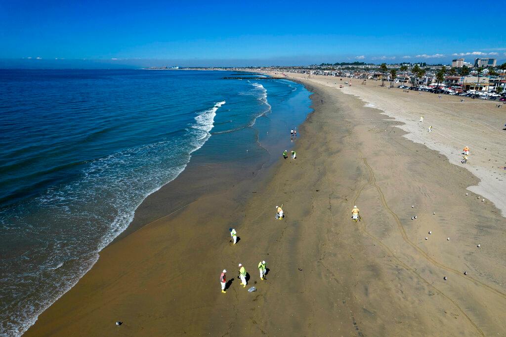 Workers clean oil from the sand south of the pier in Newport Beach, Calif., Tuesday, Oct. 5, 2021. A leak in an oil pipeline caused a spill off the coast of Southern California, sending about 126,000 gallons of oil into the ocean, some ending up on beaches in Orange County.