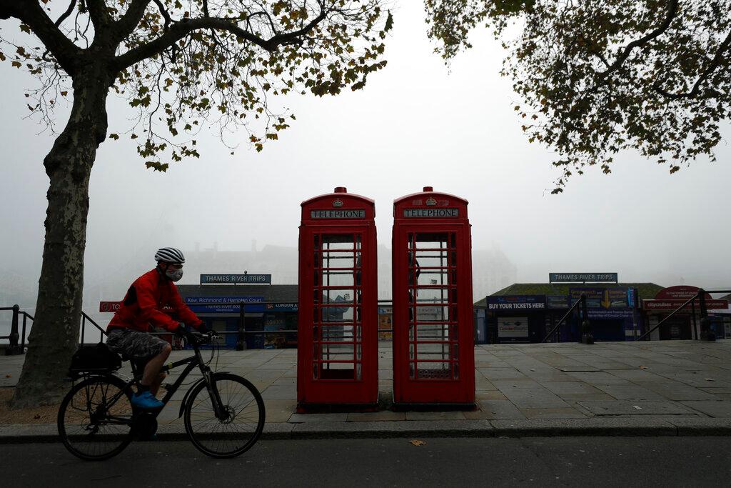 A cyclist wearing a face mask passes traditional red phone boxes, in London