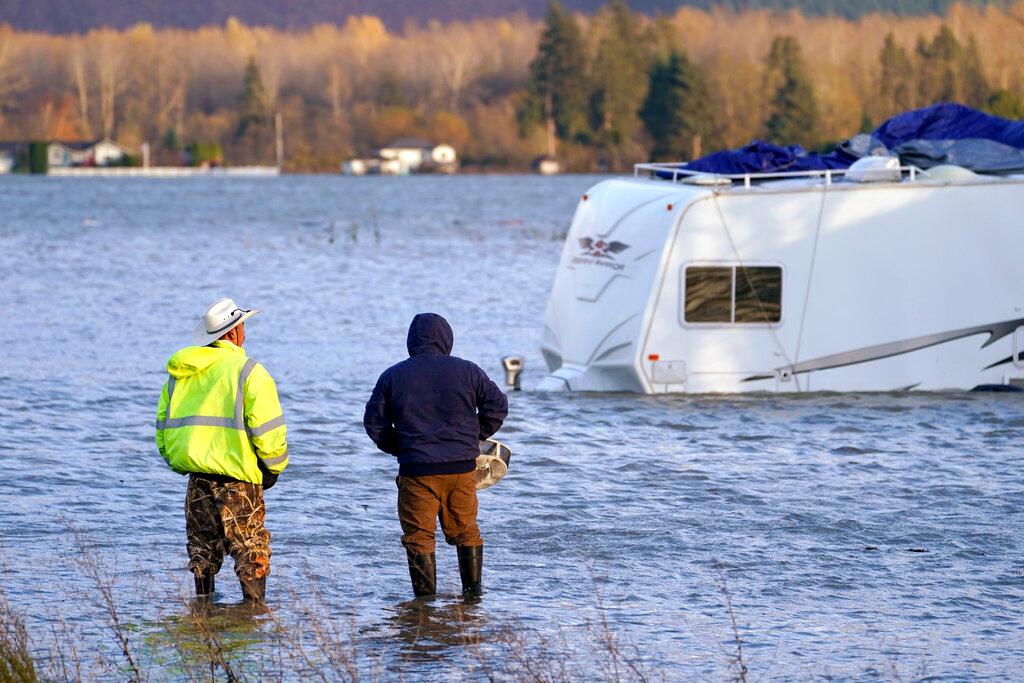 Two men stand in the flooded Skagit River and look across at an RV in Sedro-Woolley, Wash.