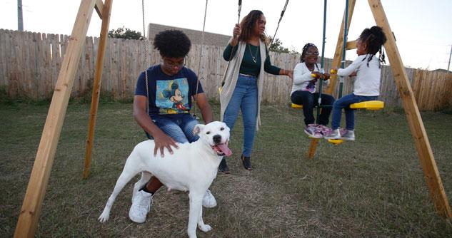 A mom and her three children on a swing set with their white dog