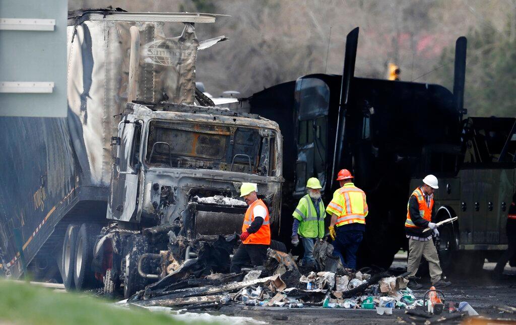 Workers clear debris from a highway following a deadly pileup involving a semi-truck hauling lumber.