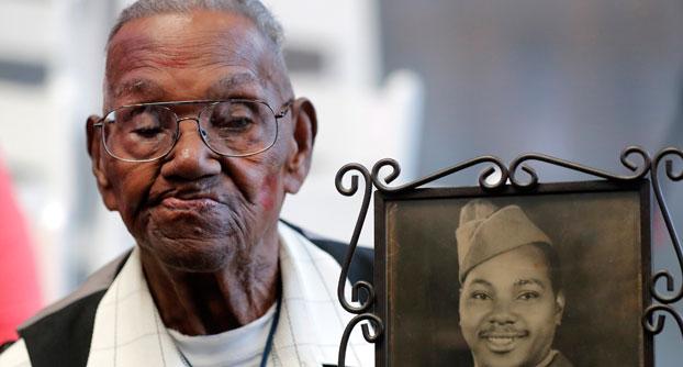 Elderly man sitting next to a portrait of himself from World War II