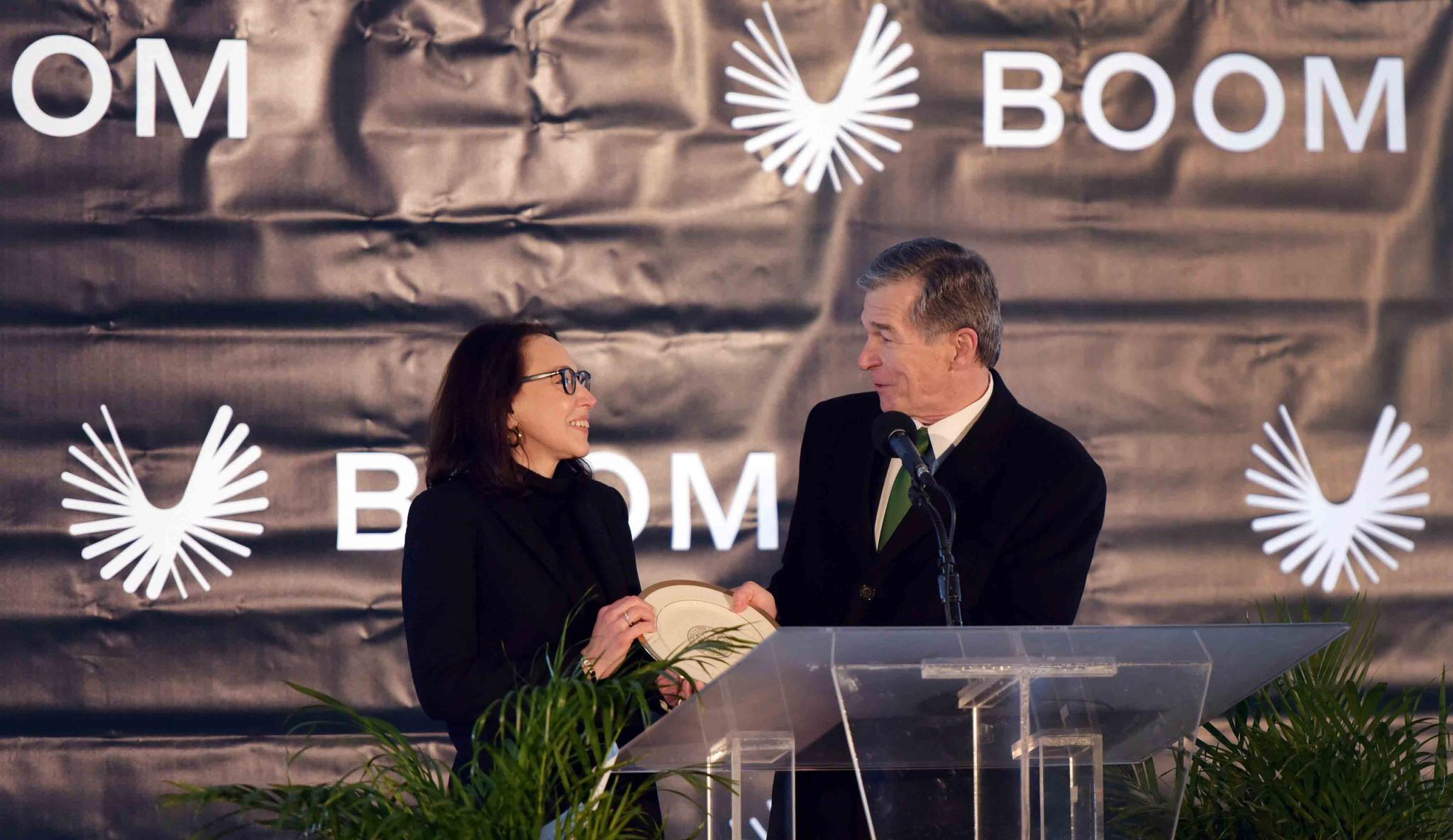 North Carolina Gov. Roy Cooper presents a gift to Kathy Savitt, President and Chief Business Officer of Boom Supersonic, during an announcement, Wednesday, Jan. 26, 2022 