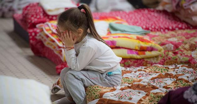 A little girl in a shelter with face in hands on a colorful blanket