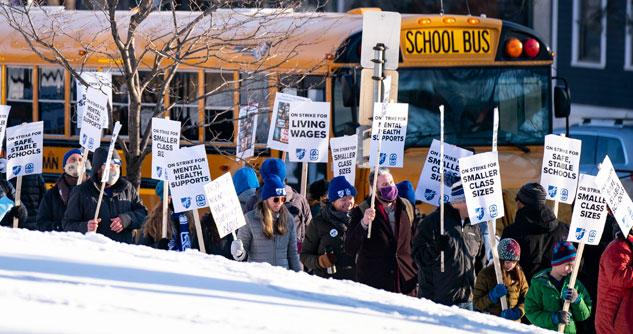 Teachers holding picket signs in front of a school bus near snow