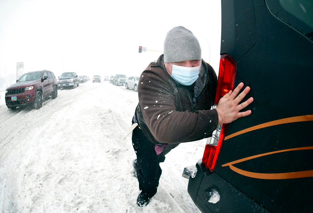 Matt Mittelstaedt, a driver for Missouri Slope Lutheran Care Center, pushes as a Good Samaritan tows the large passenger van he was driving when it got stuck in the snow in Bismarck, N.D.