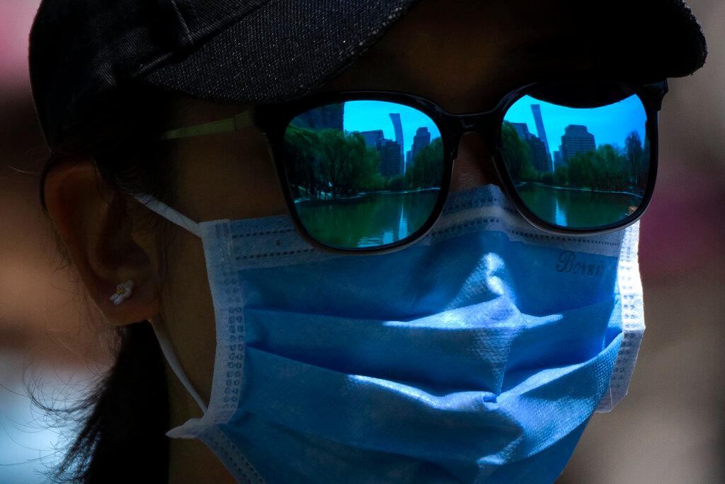 Skyline is reflecting in the sunglasses of a woman wearing a face mask as she walks at a public park in Beijing