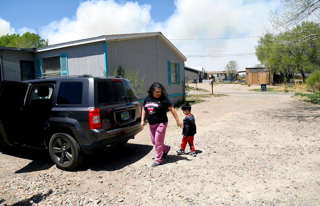 Martina Gonzales and her grandson Lukas, walk outside of their home in Las Vegas, N.M., as a plume of smoke rises in the distance