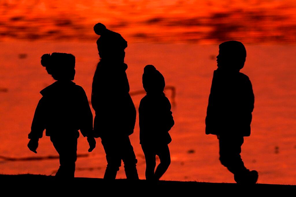 Kids are silhouetted against a pond at a park in Lenexa, Kan.