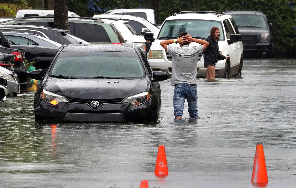 A driver climbs out of his stalled car after he tried to move it to higher ground from the flooded parking lot at the Beachwalk at Sheridan Apartments in Dania Beach, Fla., on Saturday, June 4, 2022.