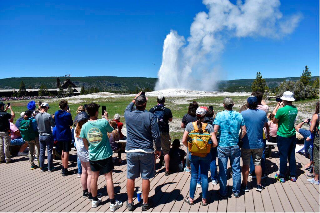The Old Faithful geyser erupts and shoots water and steam into the air as tourists watch