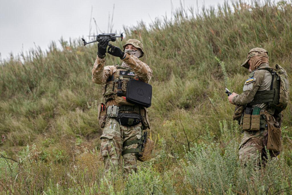 Two solders in camouflage uniforms on grassy hillside.