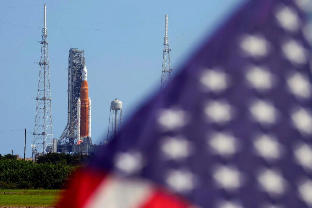Flag flying in foreground with rocket on launch pad in background