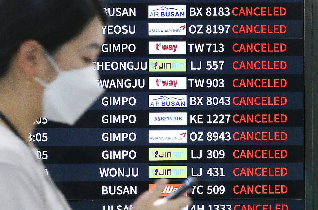 Woman checking phone with electronic board behind showing flights 