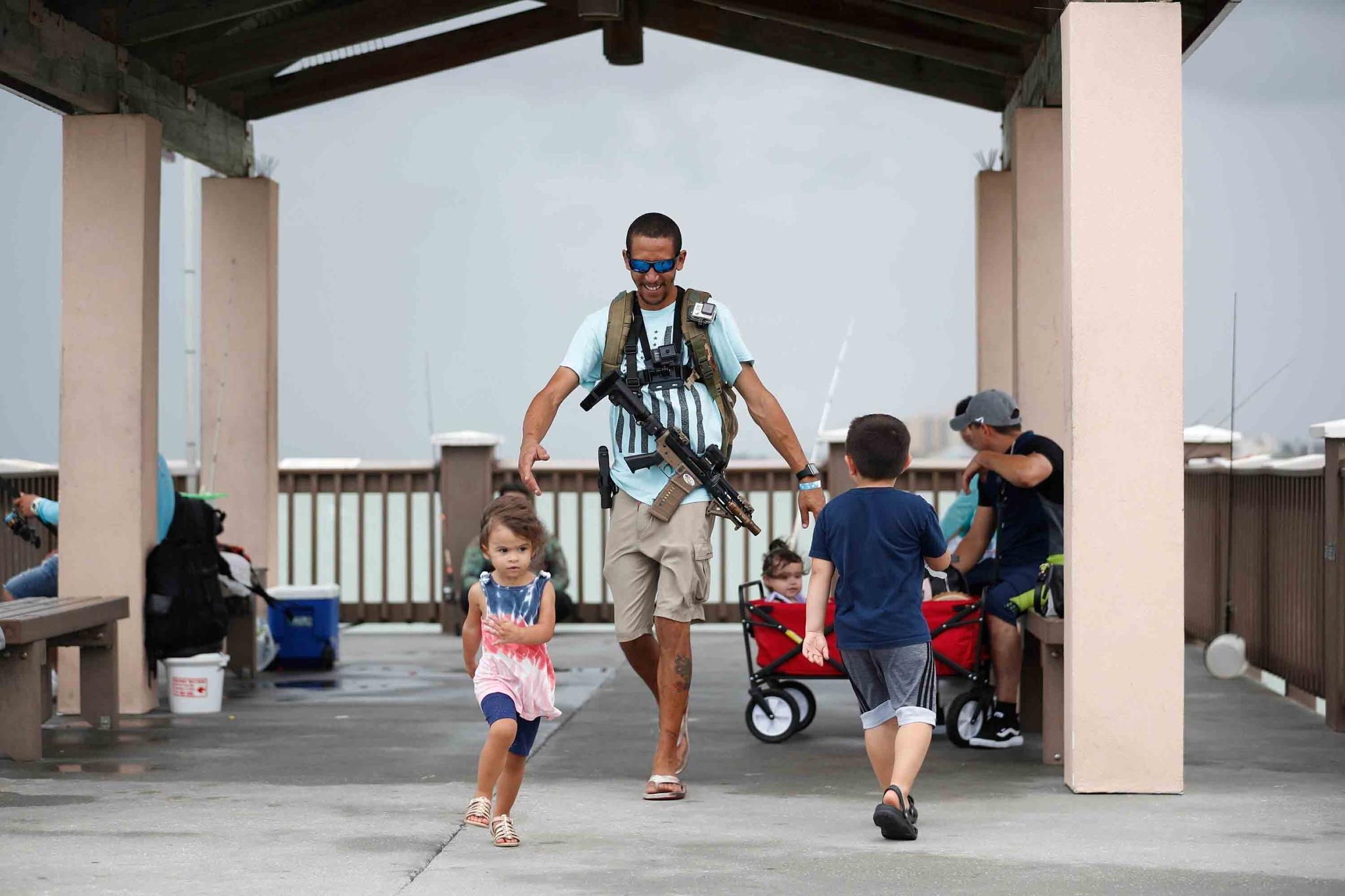 Michael Taylor, also known as "The Armed Fisherman", walks along Pier 60 in Clearwater Beach, Fla., with his 2-year-old daughter Ocean and his assault rifle and fishing gear, on July 3, 2021.