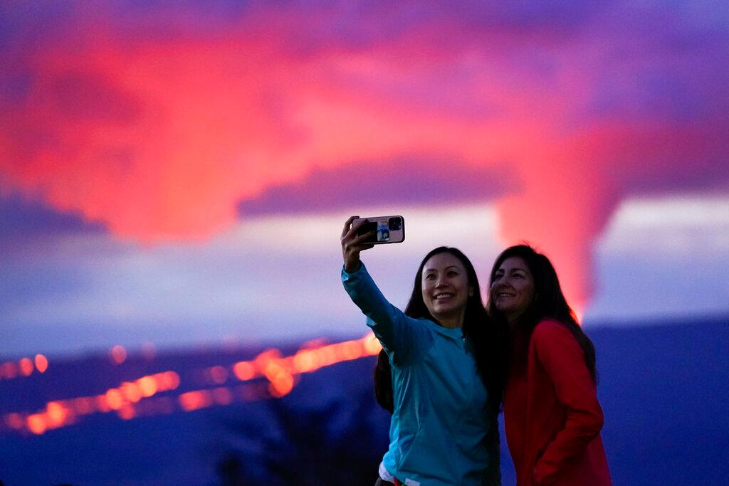 Ingrid Yang, left, and Kelly Bruno, both of San Diego, take a photo in front of lava erupting from Hawaii's Mauna Loa volcano Wednesday, Nov. 30, 2022, near Hilo, Hawaii.