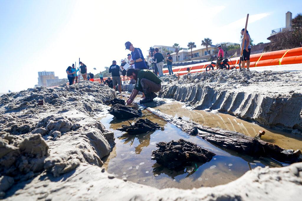 Members of a team of archaeologists study a wooden structure in the sand