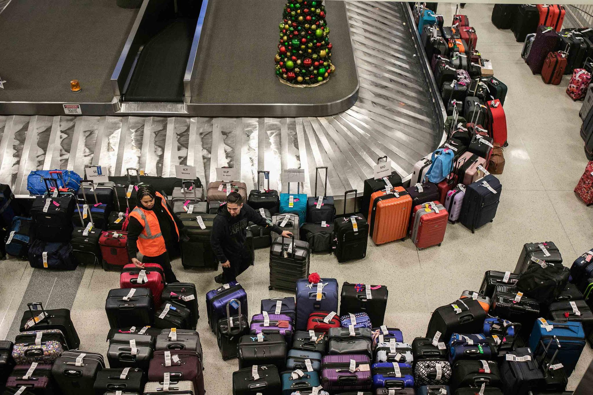 Airport staff and a person walks around a pile of lost suitcases near the baggage carousel at Midway Airport in Chicago, Tuesday, Dec. 27, 2022