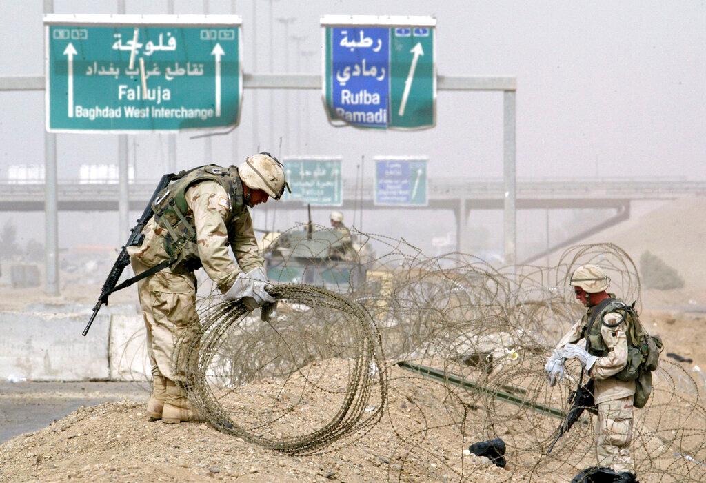 (2004) U.S. Army troops clear rolls of razor wire from the main entrance to Fallujah, Iraq